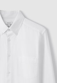 Bijela košulja slim fit kroja s gumbima, prednjim džepom, ovratnikom s gumbima i vidljivom oznakom brenda unutar ovratnika.