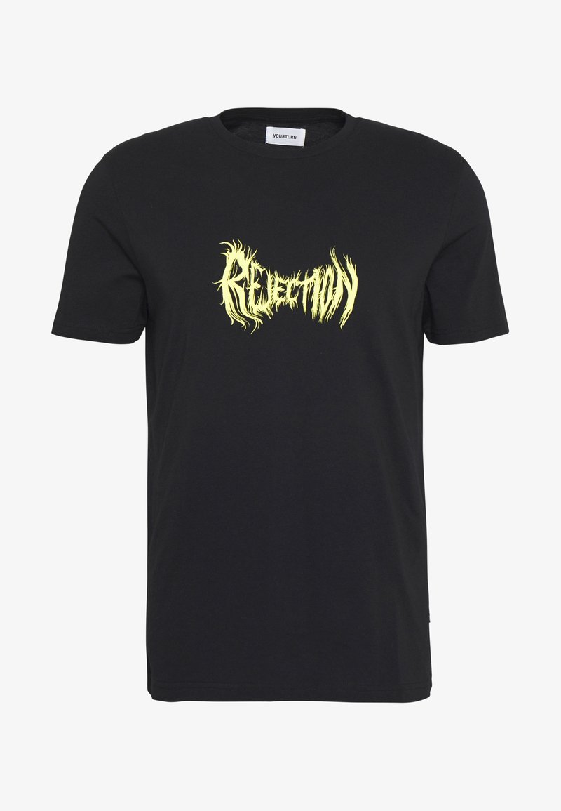 Camiseta de algodón negra con un gráfico vibrante de texto amarillo "RECHAZO" en un diseño ondulante y similar a llamas en la parte delantera. Mangas cortas, cuello redondo.