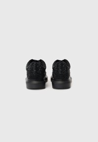 Pantofi sport negri cu un suprafață texturată, accentuată cu detalii strălucitoare, talpă amortizată și un design elegant. Vederea din spate evidențiază tocurile rotunde.