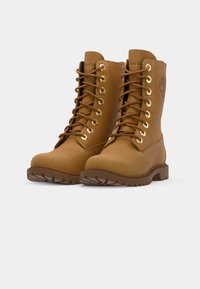 Botas de cuero marrón con cordones, ojetes dorados, suela de goma texturizada y diseño de punta redonda. Presentan un logo grabado en el lateral.