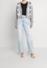 Harmaa lyhyt neuletakki, jossa on valkoisen ja sinisen väriargyle-kuvio, yhdistettynä korkeavyötäröisiin vaaleansinihin farkkuihin ja valkoisiin nilkkaketjukenkiin.