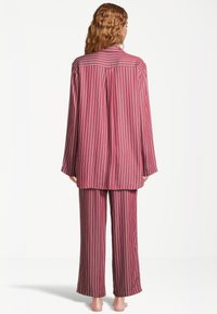 Körsbärsrödrandig pyjamas med långärmad topp och vida byxor, tillverkad av ett glatt tyg med avslappnad passform och subtil lyster.