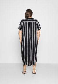 Czarna i biała w paski midi sukienka z krótkimi rękawami, luźny krój, dekolt w serek, z rozcięciem z tyłu oraz gładką teksturą materiału.