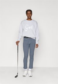Sweatshirt cinza com estampado "Golf", calças azuis estampadas, sapatos brancos, de pé com um taco de golfe. Tecido suave, estilo atlético casual.