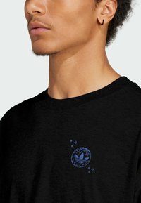 Černé bavlněné tričko s modrým grafickým logem světa se stylizovaným rostlinným motivem. Kulatý výstřih a krátké rukávy.