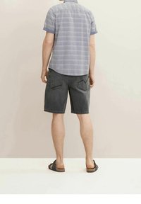 Camisa de manga corta a cuadros azul claro combinada con pantalones cortos de mezclilla gris oscuro. Los pantalones cortos tienen dos bolsillos traseros y un ajuste relajado. Sandalias negras.