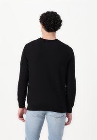 Zwarte trui met lange mouwen, ronde hals en een zak op de mouw. Gladde textuur, getailleerde pasvorm en klassiek ontwerp.