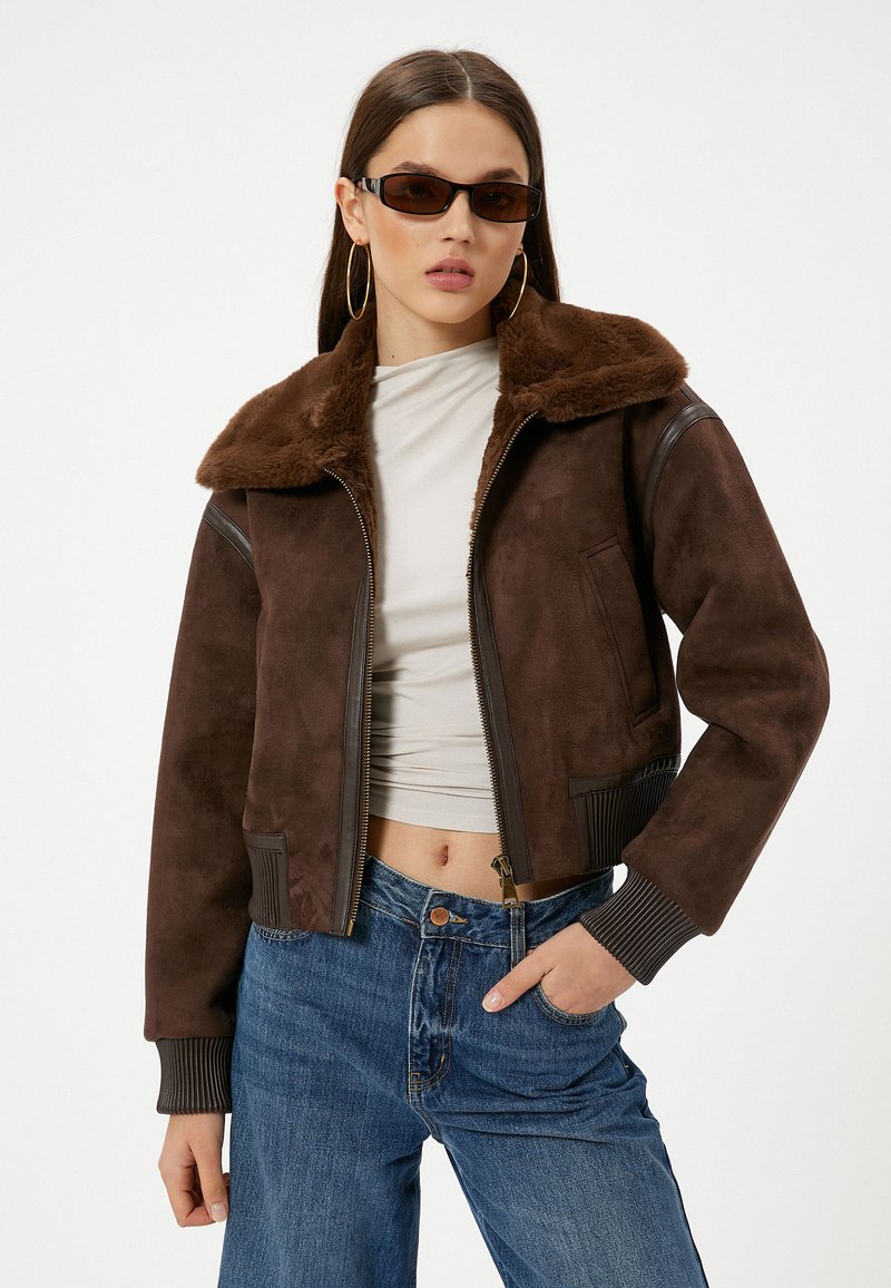 Bruine suède cropped jack met een faux fur kraag, geribde manchetten en ritsluiting. Gecombineerd met blauwe denim jeans en een lichte top.