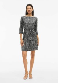 Robe à manches courtes, longueur genou ornée de sequins argentés. Présente un col rond et une taille nouée pour une silhouette ajustée.