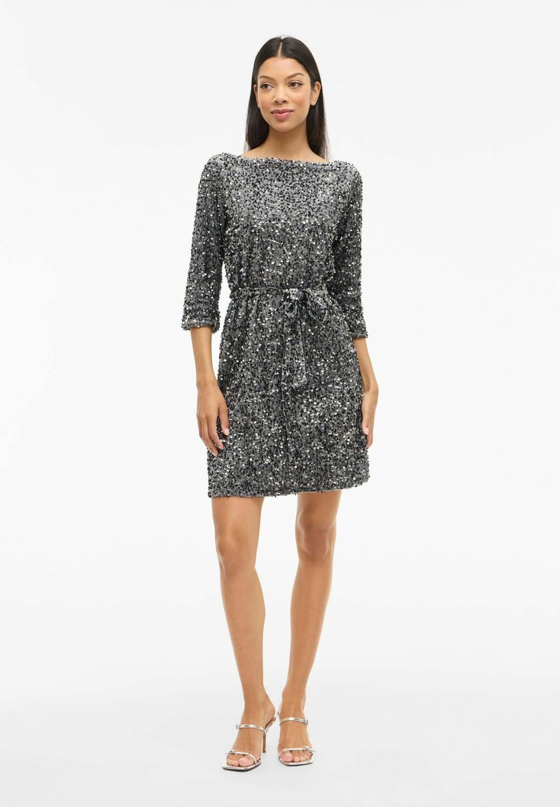 Robe à manches courtes, longueur genou ornée de sequins argentés. Présente un col rond et une taille nouée pour une silhouette ajustée.