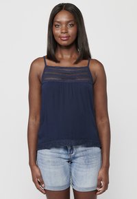 Top bleu marine à bretelles spaghetti avec un panneau en dentelle texturée sur la poitrine et une finition en dentelle au bas, associé à un short en denim clair.