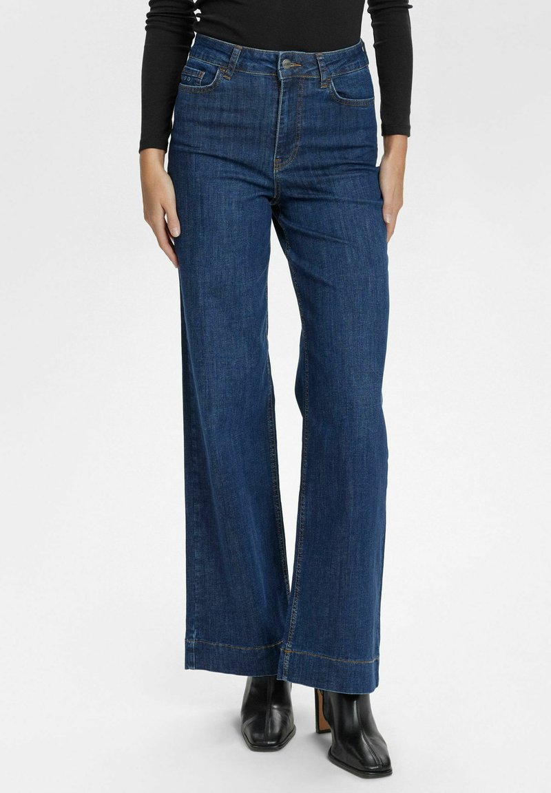 Breda ben blå denimjeans med hög midja, synlig sömnad och en polerad finish. Matchas med svarta klackade ankelskor.