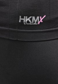 Svarta leggings med ett slätt, elastiskt tyg. Midjebandet har den broderade logotypen "HKMX by hunkemöller" i vitt med en rosa accent.