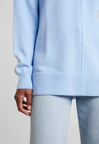 Suéter azul claro de tejido suave, con puños y dobladillo de canalé. Combinado con jeans azul claro, que muestran un corte relajado y una textura suave.