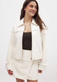 Valge denimpusa, millel on tõmblukuga esiosa, teravad kraed ja narmastega ääred, kombineeritud sobiva sätendava seeliku ja lendava tekstuuriga. Sellel on sile pind ja juhuslik lõige.