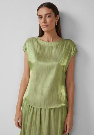 Haut vert en satin avec des manches courtes, un col rond et une coupe ample. Le tissu a une texture lisse et brillante, complétant la jupe fluide.