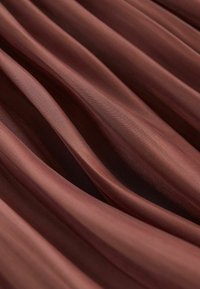 Tissu doux et lisse avec des plis profonds et réguliers dans une riche couleur marron, créant une texture fluide et stratifiée.
