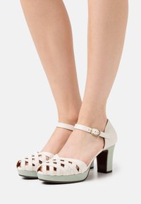 Talons fermés en cuir blanc avec des brides tissées, dotés d'une plateforme texturée vert menthe et d'une bride de cheville avec une boucle dorée.