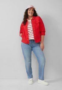 Rode denimjack over een wit met rode gestreepte shirt, gecombineerd met lichtblauwe jeans en witte sneakers. Het model draagt een lichtroze pet.