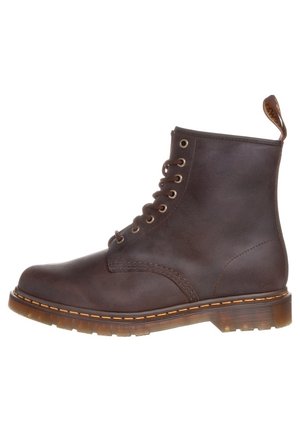 Bruine leren veterboot met dikke doorschijnende zool en gele stiksels, voorzien van een aantreklipje aan de achterkant.