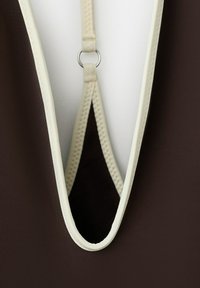 Primo piano di tessuto marrone scuro con rifinitura color crema e un anello che collega due cinturini al centro.