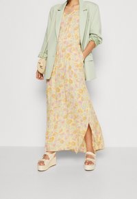 Blomster maxi kjole i gul med pink og lilla blomster, parret med en mintgrøn blazer. Platform wedges med stropper fuldender looket.