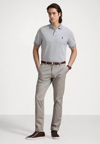 Polo rayé gris et blanc, avec un col bleu ; associé à un pantalon gris clair et des baskets marron avec une semelle blanche.