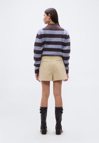 Ριγέ πλεκτό πουλόβερ σε μπλε και καφέ χρώμα, μπεζ σορτς και μαύρες μπότες μέχρι το γόνατο. Διαθέτει ριμπ υφή και δομημένο σχέδιο.