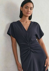 Dunkelgraues Kleid mit V-Ausschnitt, kurzen Ärmeln und gerafftem Detail in der Taille. Glattes Gewebe mit einer weichen, fließenden Textur.