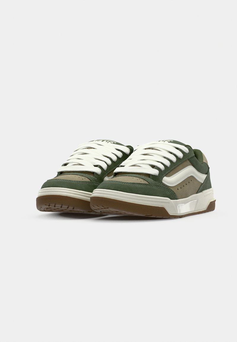 Sneaker verde oliva con lacci bianchi, pannelli lisci e testurizzati, suola in gomma e perforazioni sottili. Design casual con accenti a contrasto.