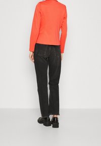 Veste ajustée corail à manches longues, associée à un jean noir taille haute et des chaussures noires épaisses. Design simple et structuré sans ornements.