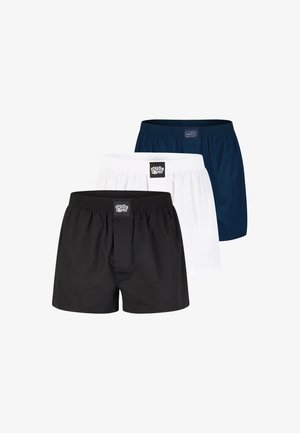 Schwarze Boxershorts aus einem leichten Stoff mit einem elastischen Bund, versehen mit einem Logo auf der Vorderseite. Das Modell steht oberkörperfrei vor einem neutralen Hintergrund.