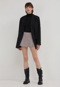 Blazer oversize nero sopra un dolcevita nero, abbinato a una mini gonna plissettata grigio chiaro e stivali neri al ginocchio con fibbie.