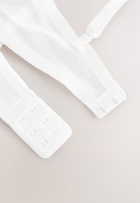 Baltos reguliuojamos liemenėlės petnešėlės su tekstūruotu tinklelio dizainu, turinčios stačiakampę kabliuko ir kilpos užsegimą su keliomis tvirtinimo galimybėmis.