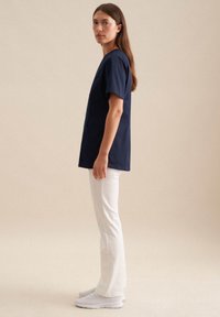 T-shirt in cotone navy a maniche corte, vestibilità comoda, con dettaglio della tasca frontale, abbinato a pantaloni bianchi a zampa d'elefante e scarpe da ginnastica bianche.