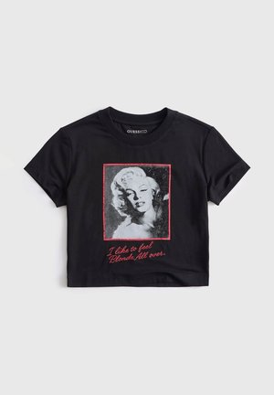Zwart cropped T-shirt met een zwart-witte foto van een blonde vrouw, omlijst in rood, en rode tekst met de tekst "I like to feel Blonde All over."