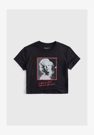 Zwart cropped T-shirt met een zwart-witte foto van een blonde vrouw, omlijst in rood, en rode tekst met de tekst "I like to feel Blonde All over."