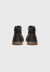 Botas de tobillo de cuero negro con cuello elástico texturizado y cremalleras laterales. La suela de goma proporciona tracción. Superficie suave con costuras a tono.