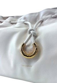 Borsa a mano in pelle bianca con chiusura a cordoncino annodato e un accento in metallo circolare dorato. Il marchio è impresso nella parte inferiore.