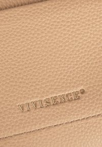 Superficie de cuero beige con textura y marca en relieve dorado "VIVISENCE®", con una costura horizontal visible cerca de la parte inferior.