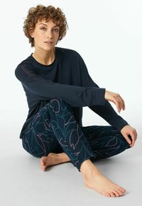 Dark long-sleeve shirt paired with tapered pants featuring a navy background and floral pattern in teal and pink. Soft fabric, relaxed fit.