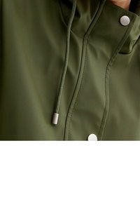 Oliwkowa wodoodporna kurtka z wysokim kołnierzem, srebrnymi zatrzaskami i regulowanym sznurkiem. Gładka tekstura z widocznymi szwami.
