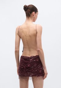 Vīnogsarkanā mini kleita ar atvērtu muguru, rotāta ar ziedu izšuvumiem, spīdumiem un pērlīšu bārkstīm apakšmalā. Plānas spaghetti siksniņas.