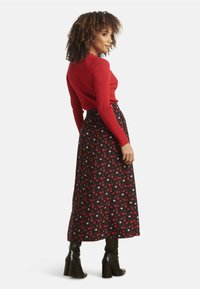 Red ribbed long-sleeve top paired with a black maxi skirt featuring red and pink dot patterns. Model wears black heeled boots.