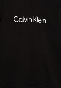 Sweat-shirt noir en tissu doux avec un logo "Calvin Klein" blanc centré sur la poitrine. Design simple, sans motifs ni accents supplémentaires.