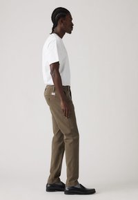 Brown straight-leg trousers paired with a white t-shirt; black shoes; noticeable pocket details and stitching. Smooth fabric texture.