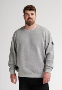 Grijze sweatshirt met een gestructureerd ruitpatroon, geribde manchetten en een ronde hals, gecombineerd met donkere jeans.