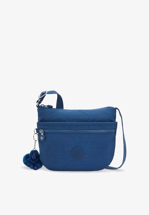 Bolso azul de estilo bandolera con correa ajustable, bolsillo frontal con cremallera, logotipo redondo y un pequeño llavero de mono azul peludo adjunto.