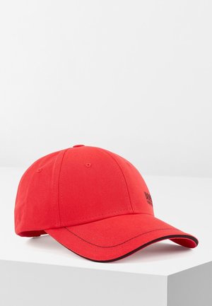 Rød baseballkasket med sort kant på den buede skygge, placeret på hvid overflade mod almindelig hvid baggrund.