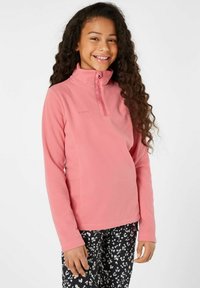 Sudadera de forro polar rosa con un cuello alto, cierre de media cremallera en la parte delantera y una textura suave. Combinada con pantalones negros que tienen un patrón floral blanco.